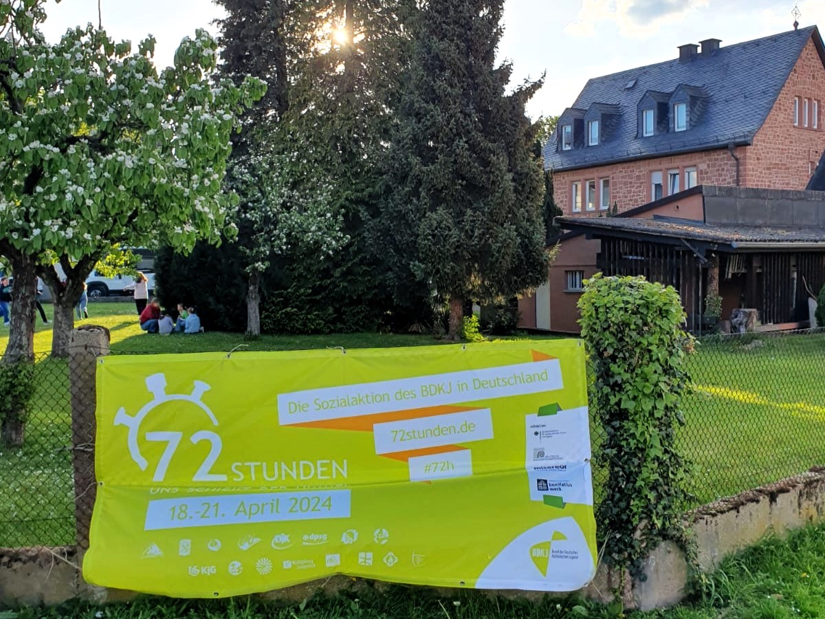 Banner 72Stunden Aktion vor dem Pfarrgarten. Im Hintergrund das Pfarrhaus