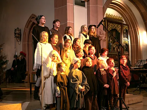 Kinder in Gewändern für das Krippenspiel stehen in der Kirche und singen