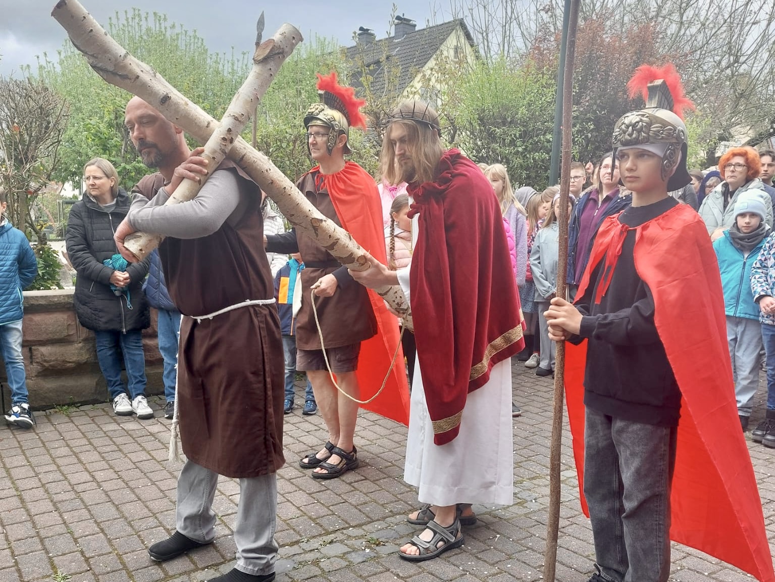 Ein Mann als Simon trägt das Kreuz, Jesus und zwei Soldaten stehen dahinter