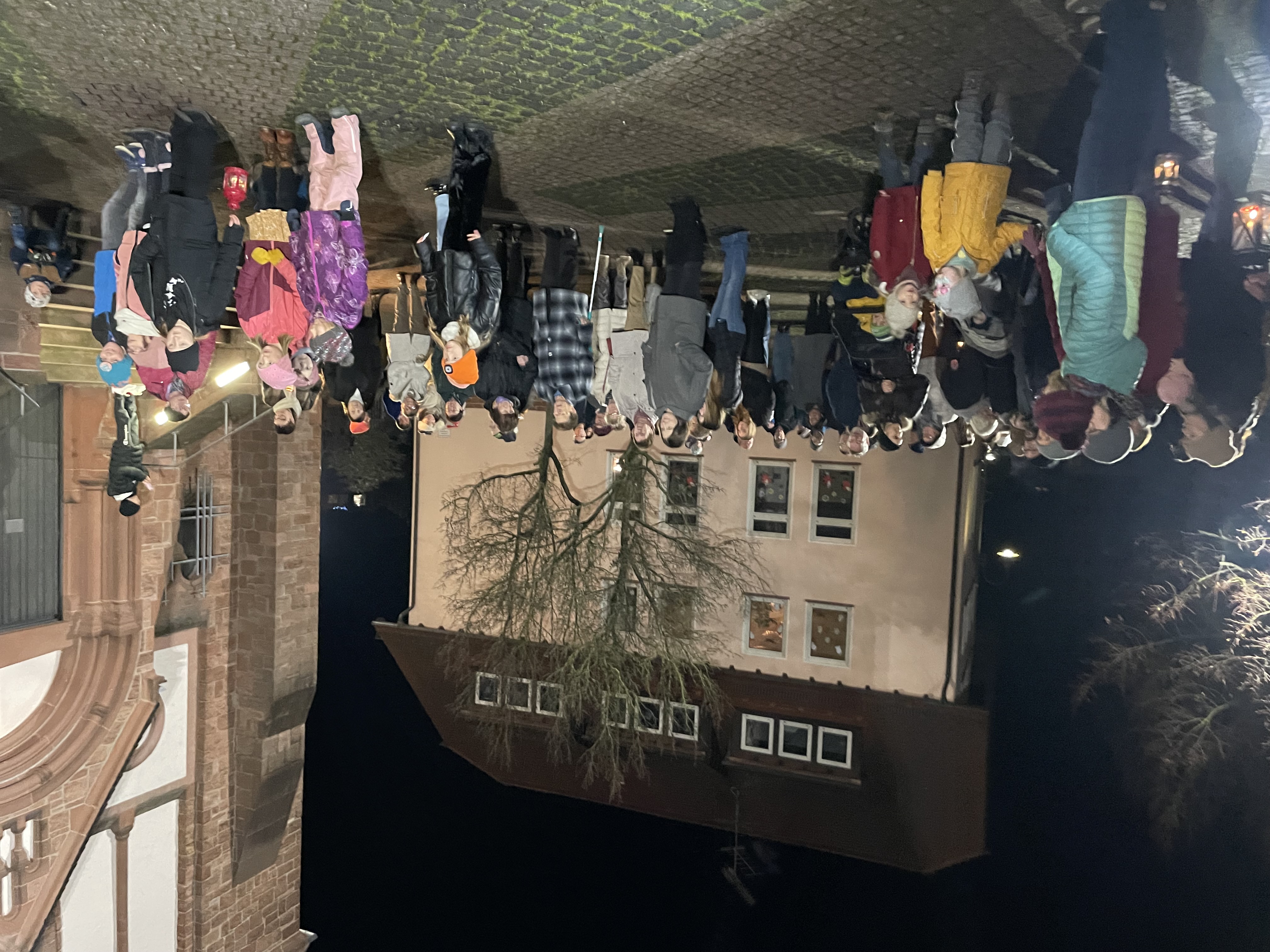 Viele Erwachsene und Kinder stehen in der Dunkelheit auf dem erleuchteten Kirchplatz.