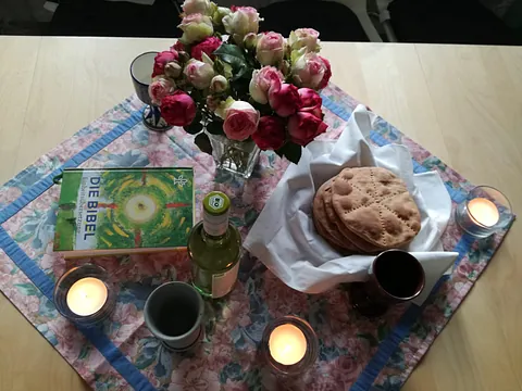 Tisch mit Blumen, Bibel, Fladenbroten, Becher und Kerzen