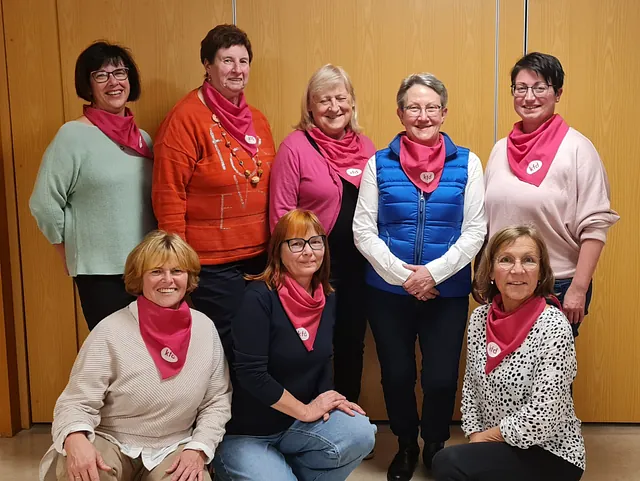 8 Frauen mit purpurfarbenen kfd-Tüchern lachen freundlich.