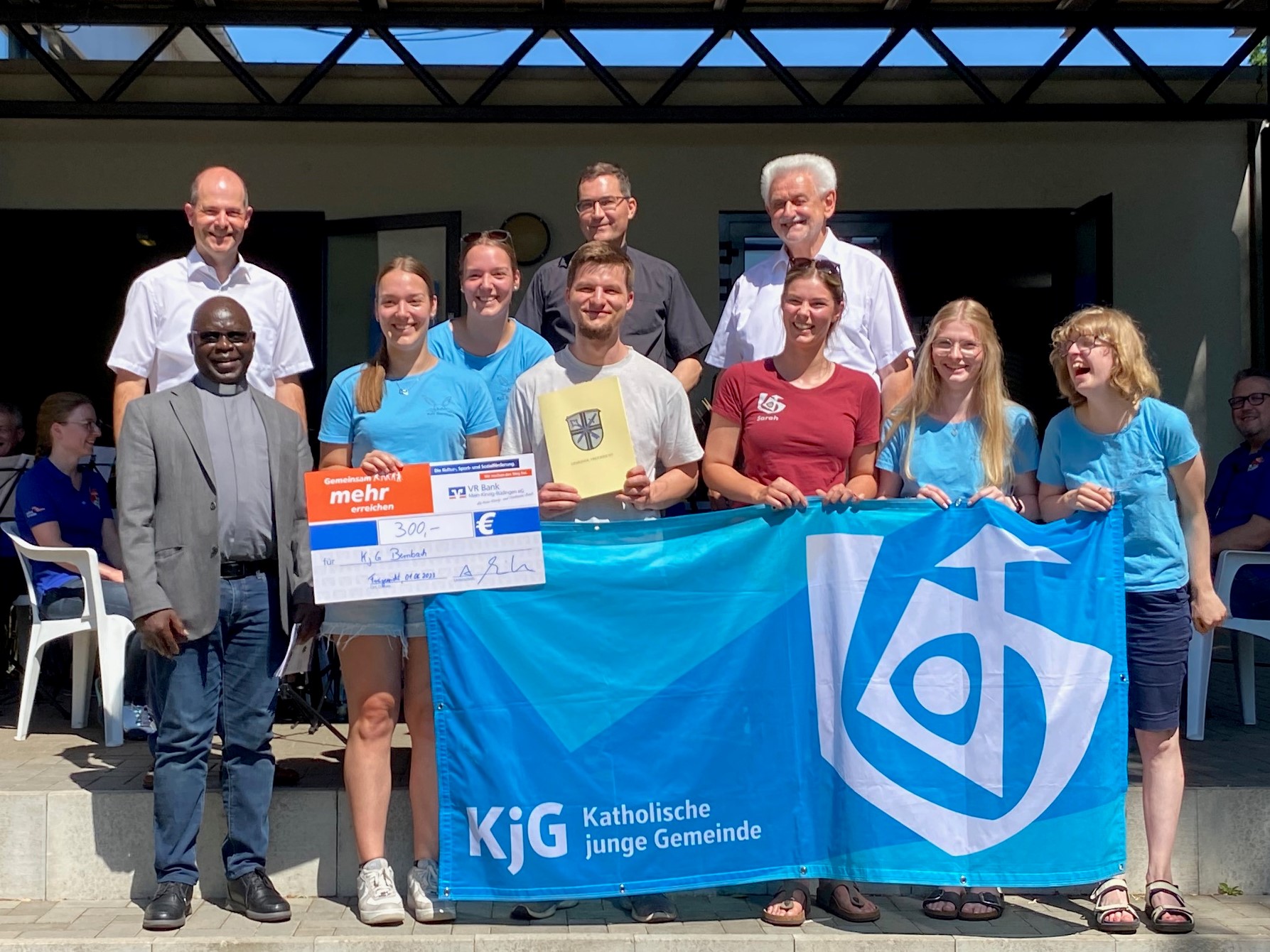 6 Jugendliche halten das Banner der kjg und einem großen Scheck der VR-Bank. mit 2 Pfarrern und 2 Gemeindevertretern.