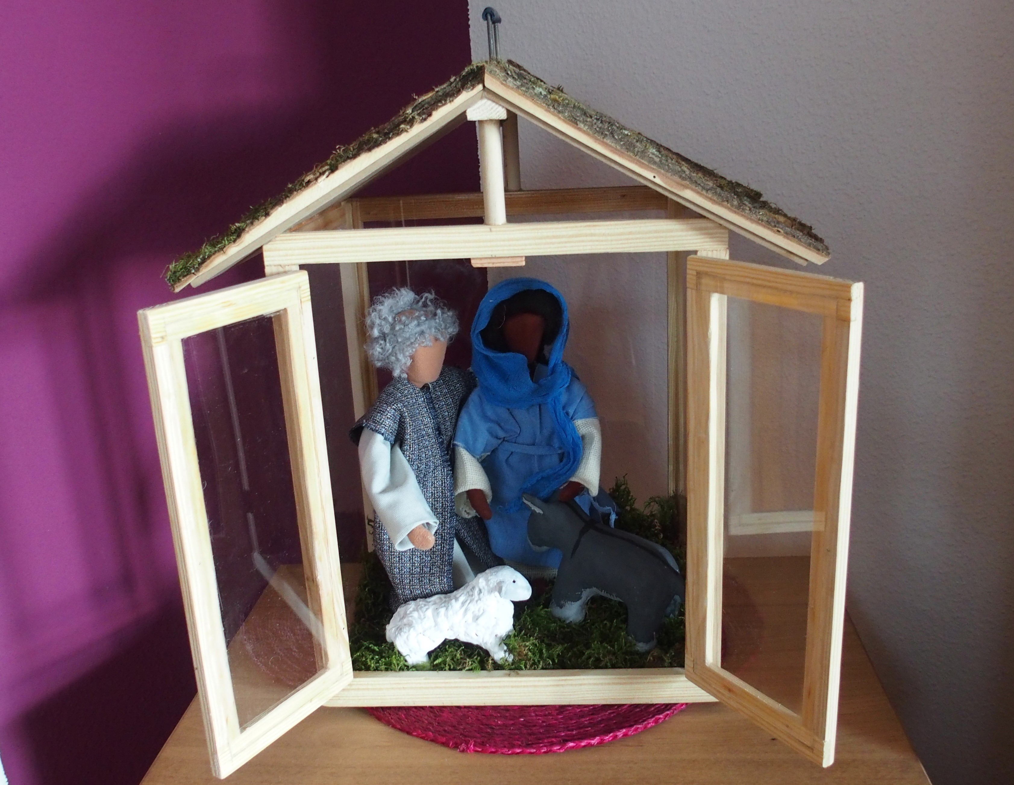 Häuschen aus Holz mit geöffneten Türen, darin stehen Figuren von Maria und Mosef, Esel und Schaf