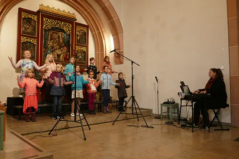 Kinderchor in der Kirche singt mit Gesten, Chorleiterin am Keyboard